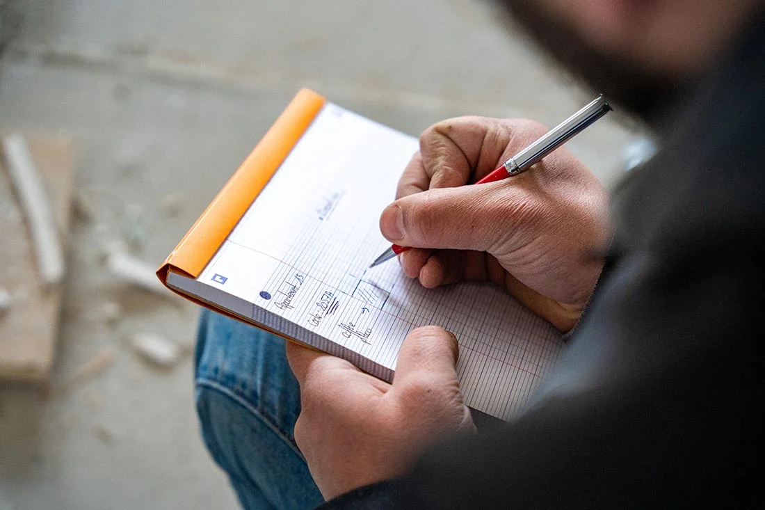 Une main prenant des notes techniques dans un carnet, illustrant la recherche et l'acquisition de connaissances